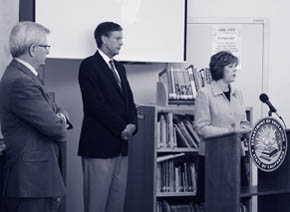 Three education leaders speak at a podium in a school library.